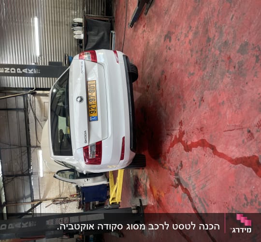 רכב לבן במוסך על רצפת בטון אדומה